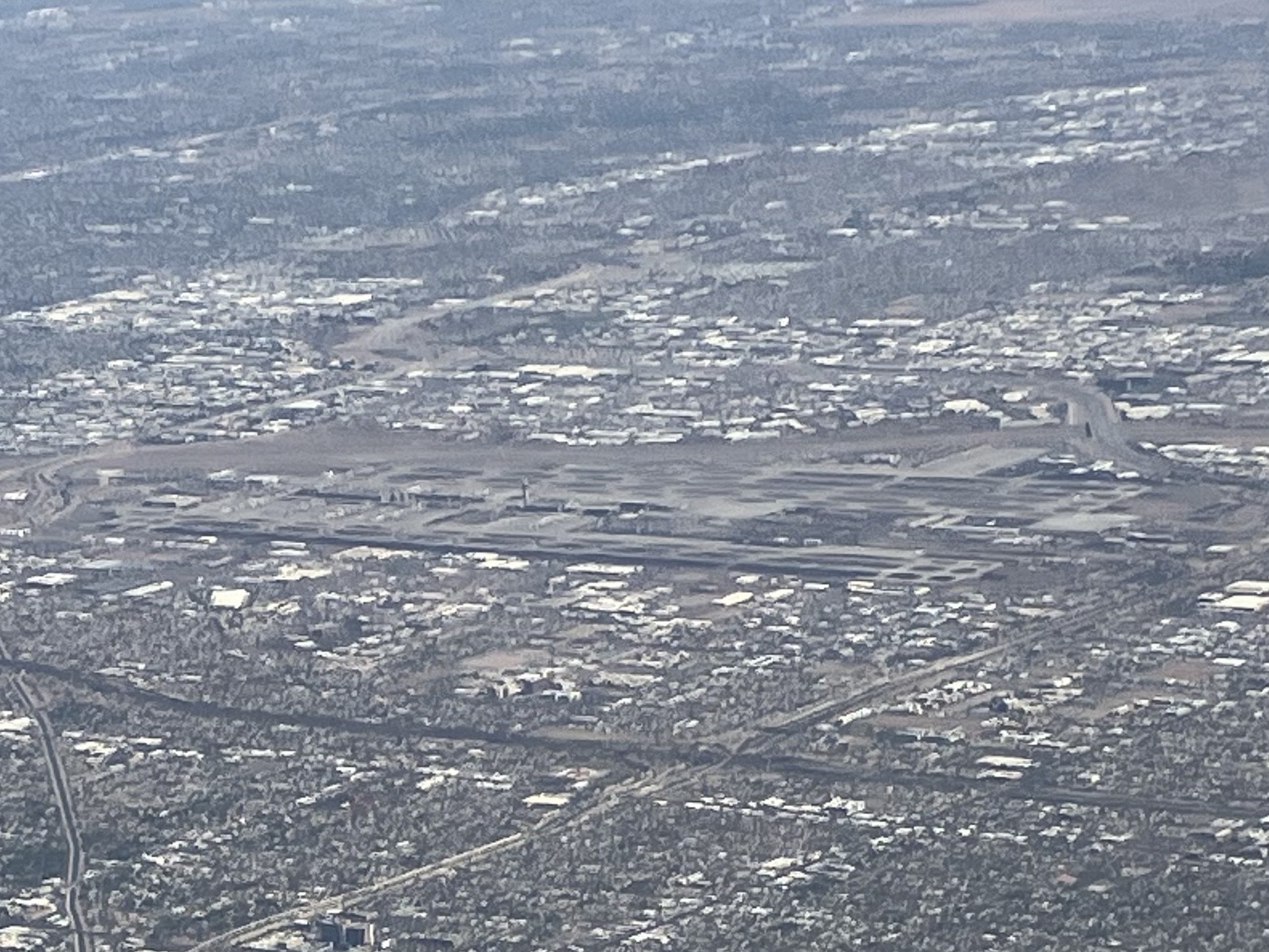 Aerial photograph of Phoenix Sky Harbor International Airport in May 2025, with Terminal 4 and its concourses in the foreground and Terminal 3 beyond, aircraft at the gates and the runways behind