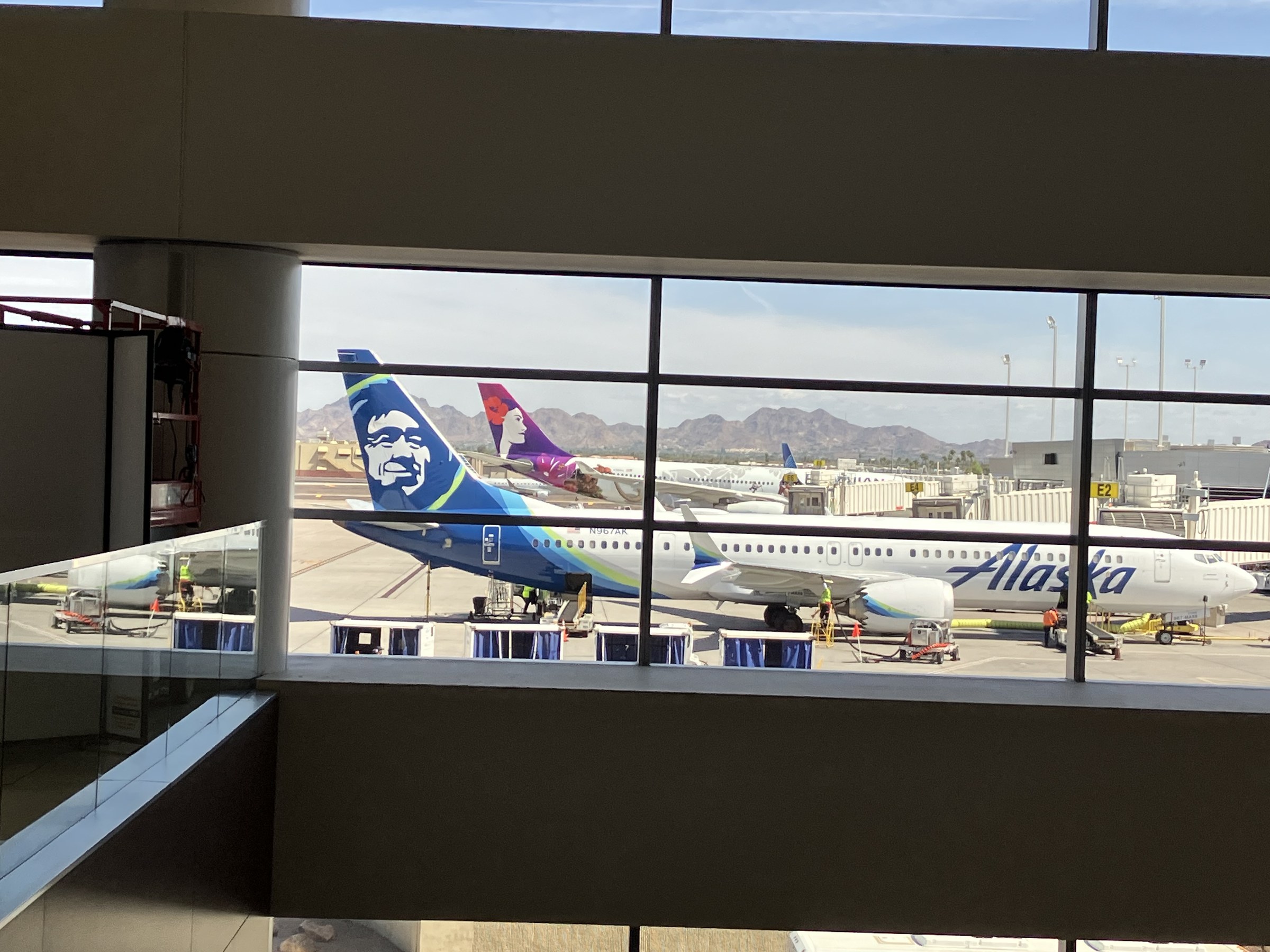 Photograph of Alaska Air Group aircraft parked at Terminal 3 gates at Phoenix Sky Harbor in April 2025, seen from inside the concourse through the gate windows
