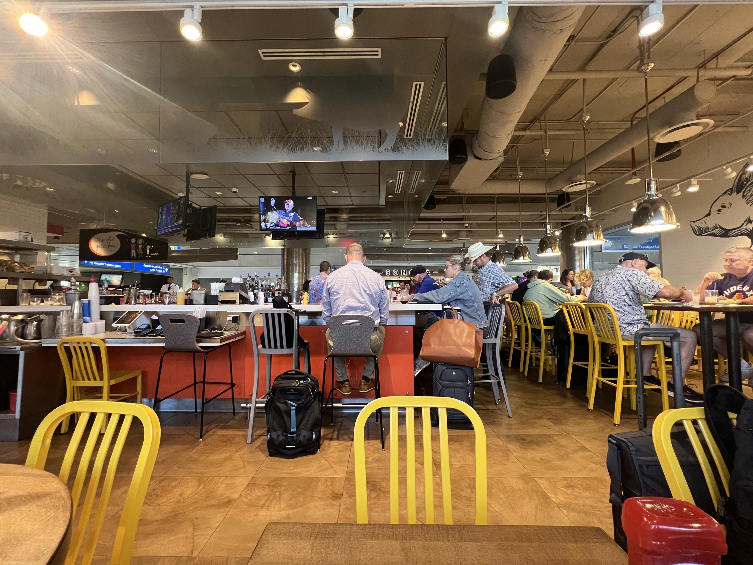 Interior photograph of a Terminal 4 concourse dining area in August 2023, with seating, food counters and overhead signage