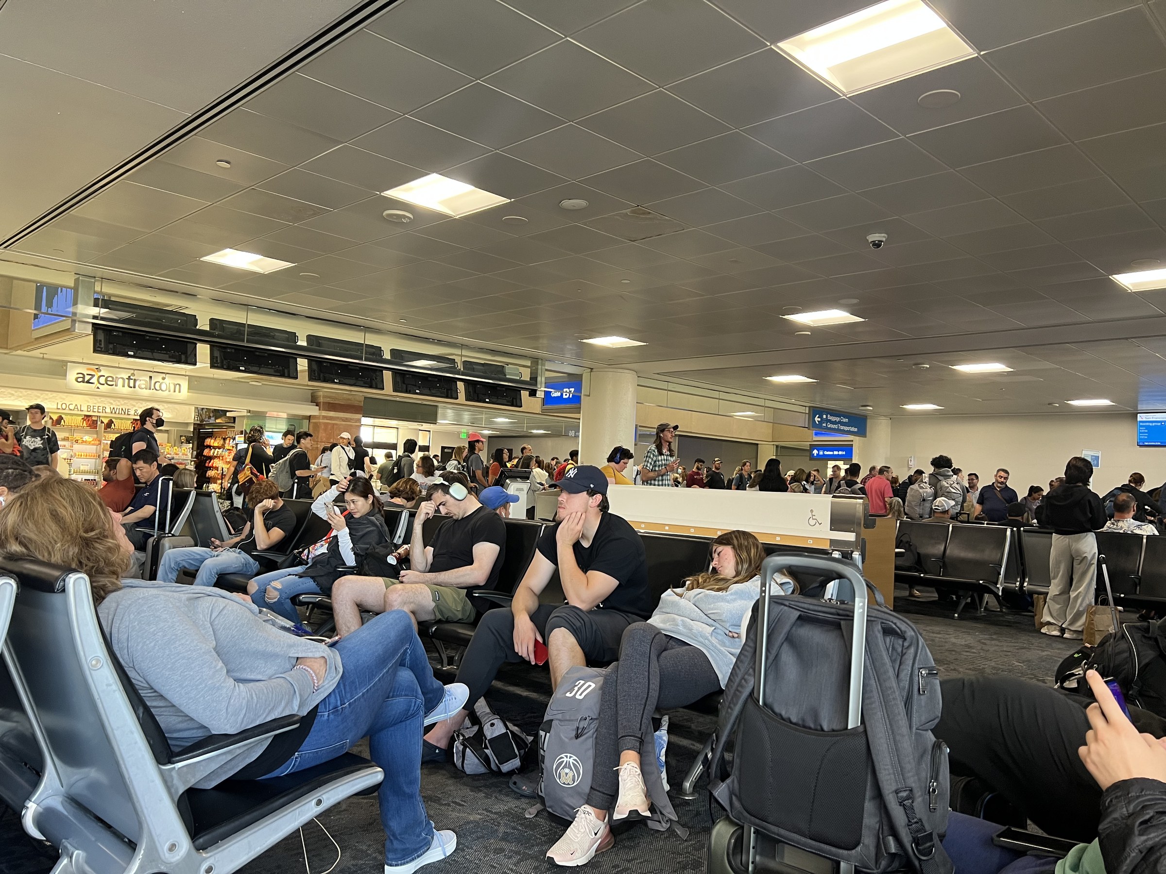 Interior photograph of a Terminal 4 gate hold room at Phoenix Sky Harbor in August 2023, with rows of seating, windows onto the apron, and the concourse ceiling above